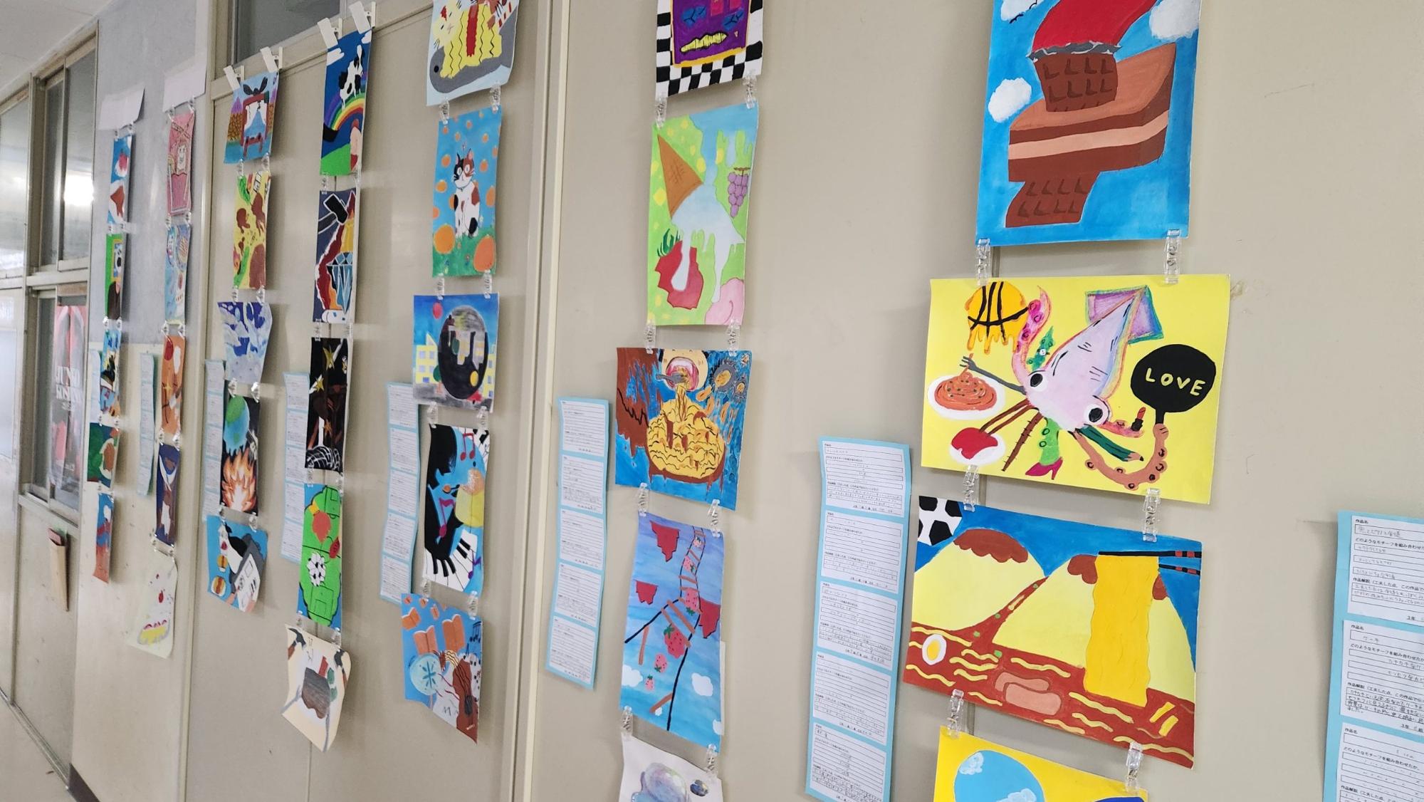 廊下の壁に3年の生徒が美術の授業で制作した5枚ずつのデザイン画と作品名などの詳細が展示されている写真