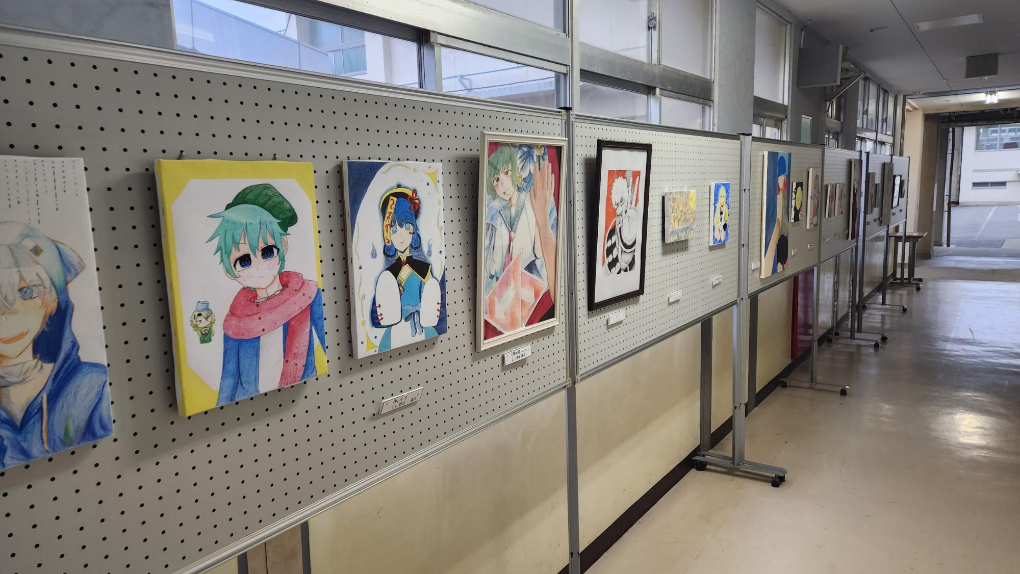 廊下の窓ガラス側に設置された掲示ボードに、美術部の生徒が描いた作品が展示されている写真