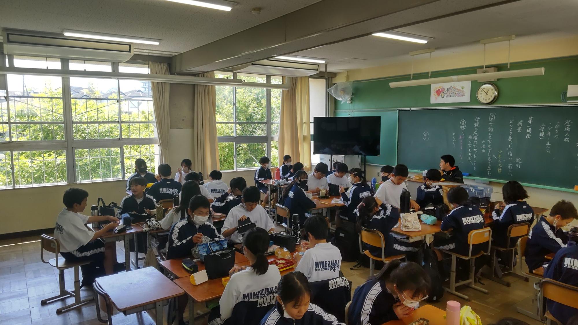 教室内で机をくっつけて班ごとに体操着姿の生徒たちが座りお弁当を食べている様子の写真