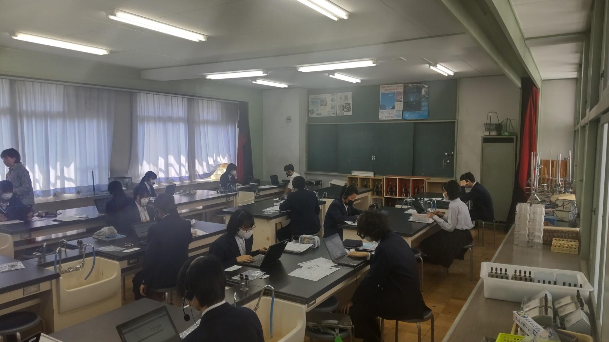 理科室のテーブルの席に2名ずつ斜めの席に座り頭にヘッドセットをした生徒たちがパソコンの画面を見ている、話すこと調査のテスト中の様子の写真