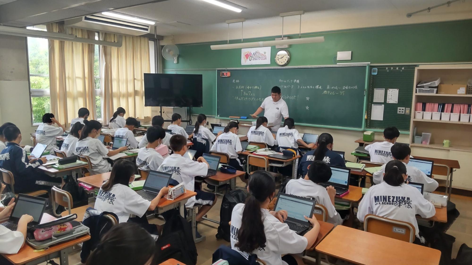自席に座った体操着姿の生徒たちが机の上に置いたタブレットを開き男性教師の授業を受けている、公開授業期間中の授業の様子の写真