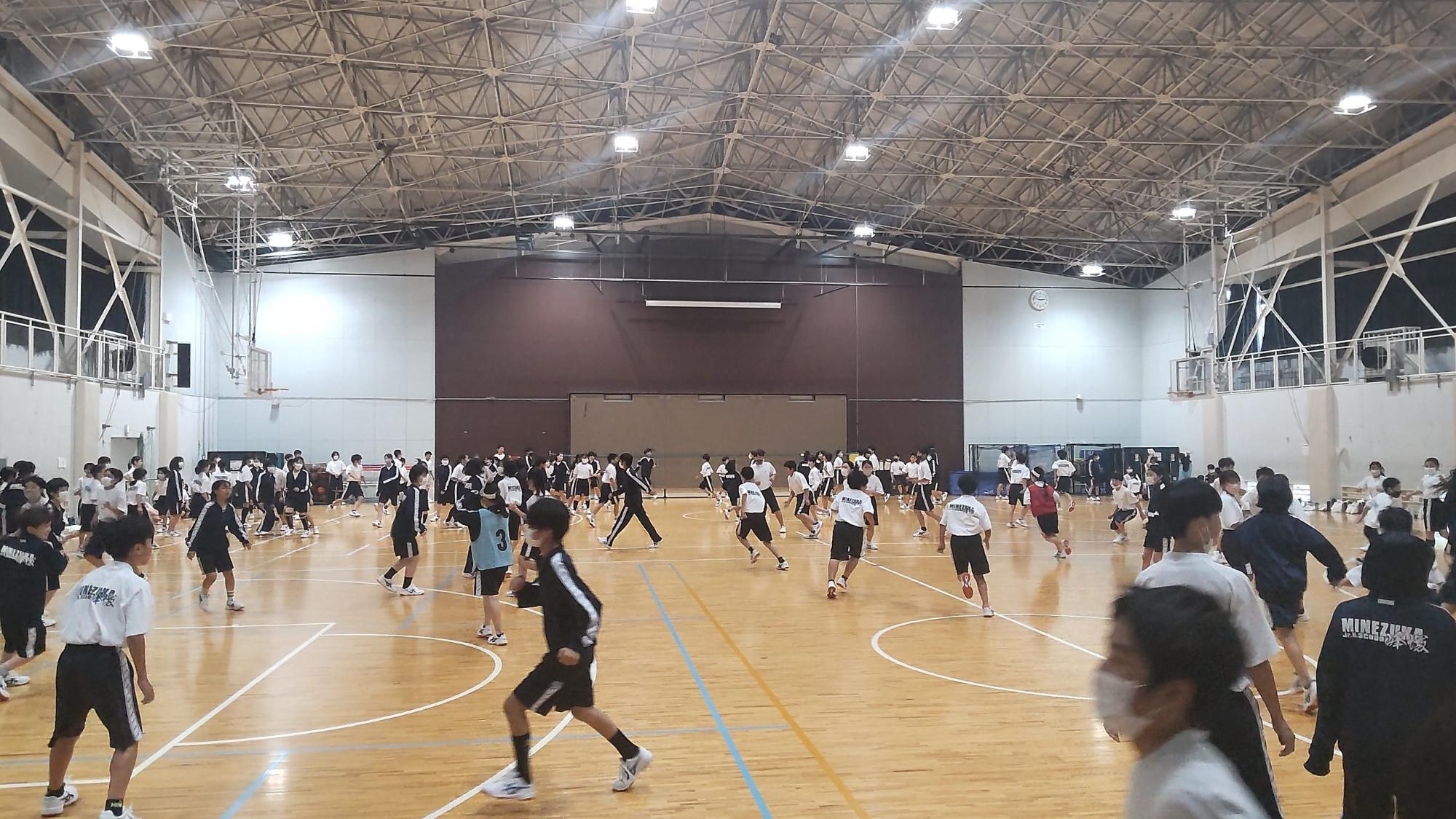 体育館内で生徒たちが鬼のお面をつけた生徒から逃げている1年生全員で鬼ごっこを行っている学年レクの様子の写真