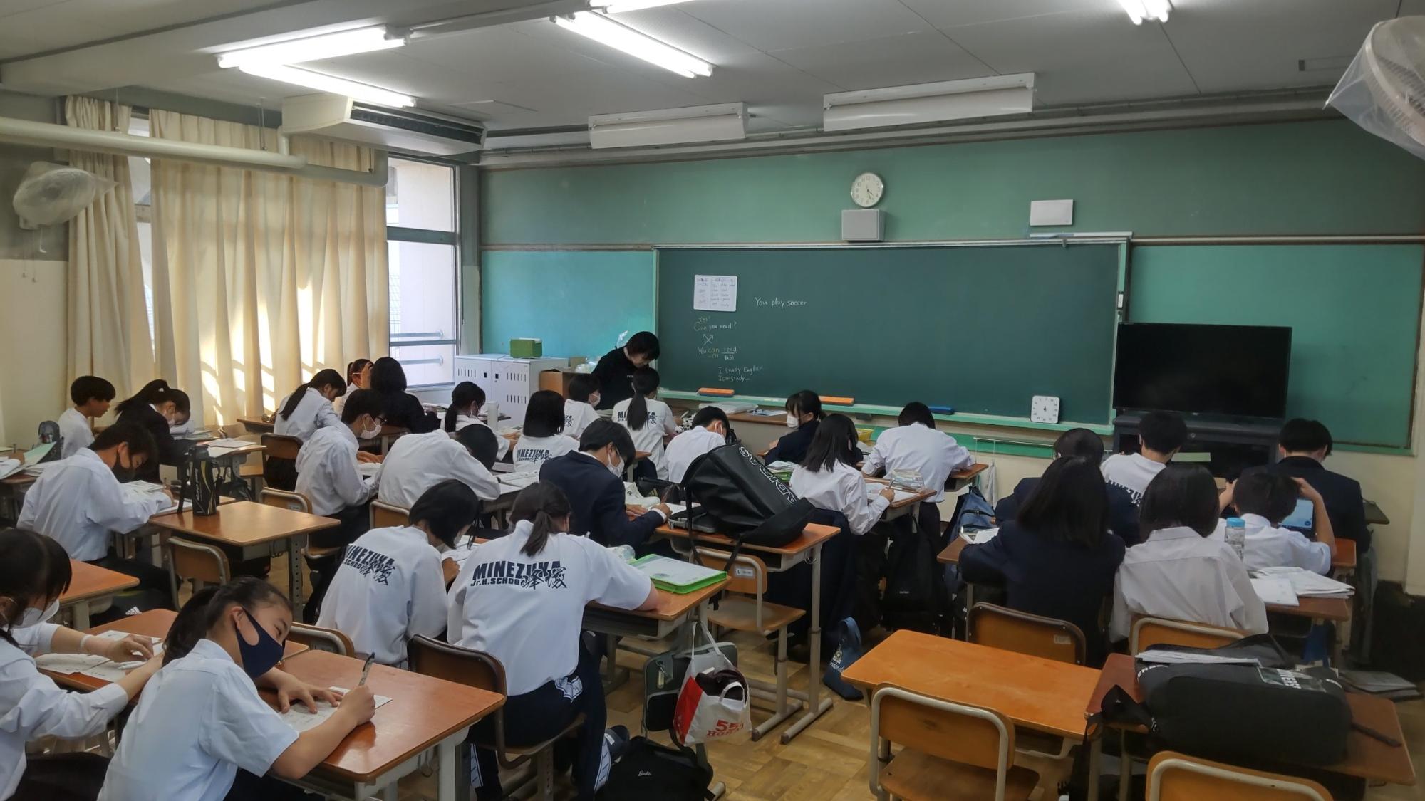 1年生の生徒たちが友達同士で教えあったり、女性教師に質問して思い思いに勉強しているテスト前勉強会の様子の写真