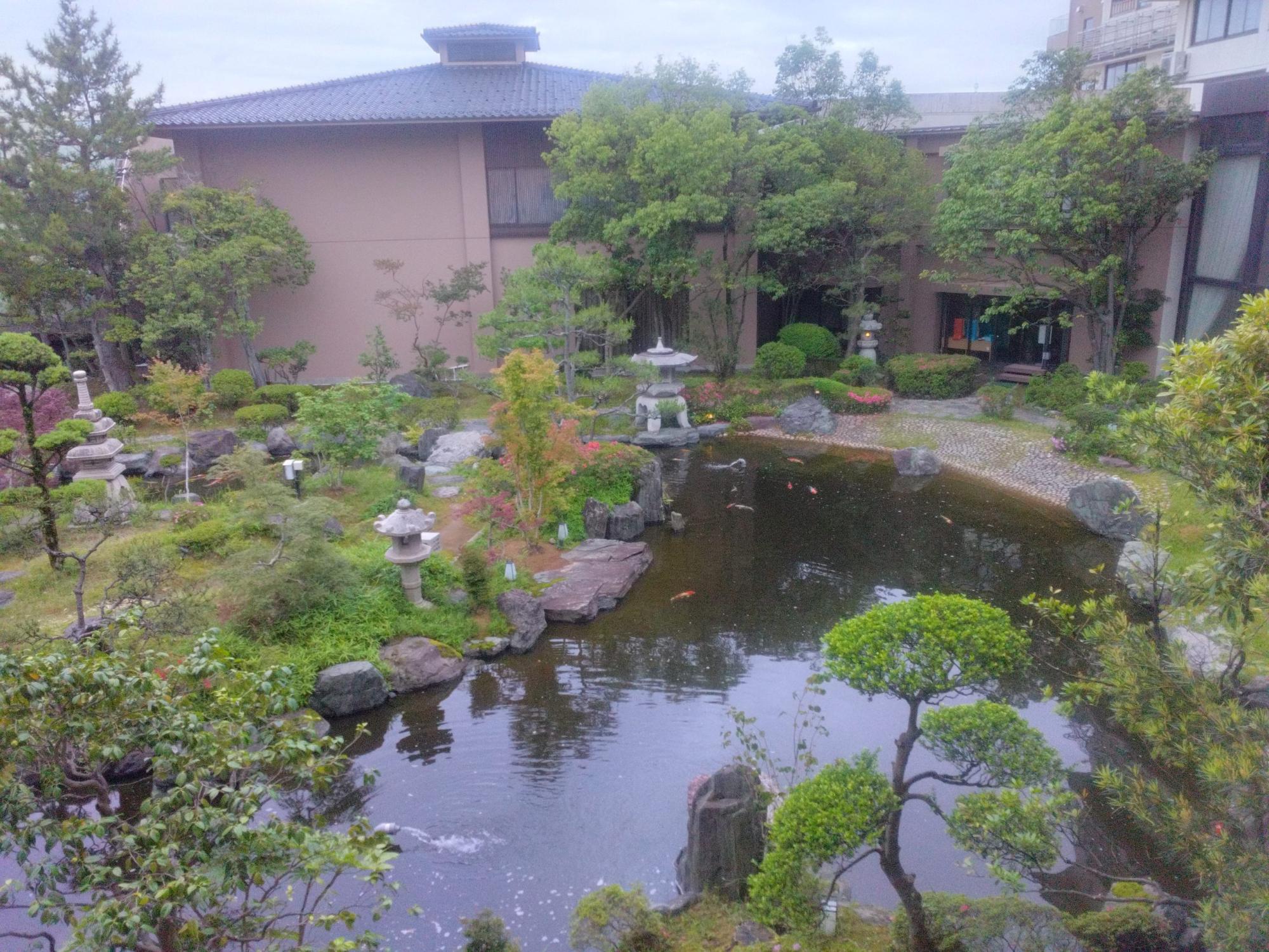 宿の傍に木々が立ち手入れが行き届いた植木や形の違う石灯篭が設置され、鯉が泳いでいる池のある日本庭園の写真