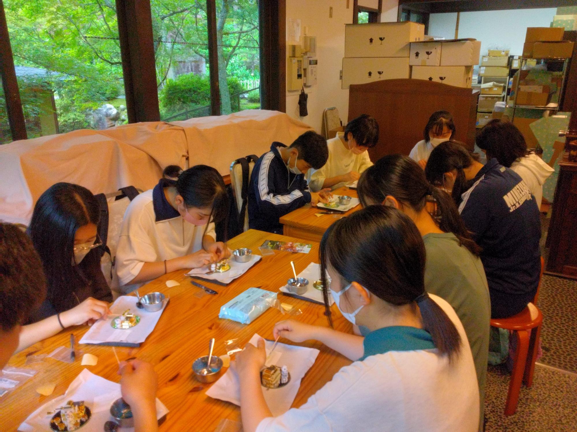 女子生徒が銀色の円形のプレートの上に思い思いに飾り付けを行っている伝統工芸体験を行っている様子の写真