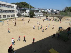 広々とした運動場で子どもたちがジャングルジムの遊具にのぼったり、運動場を走り回ったり、思い思いに遊んでいる様子を写した写真
