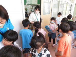 1年生の子どもたちが職員室前に集まっており、職員室の入り口で女性の先生が、集まった子どもたちと話をしている様子の写真