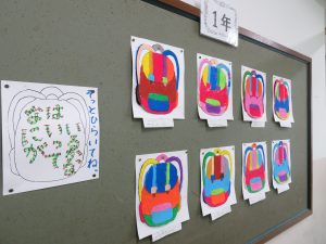 掲示板に「1年」と表示がされ画用紙にクレパスで綺麗に色塗りされたリュックサックの作品が8枚掲示されている写真