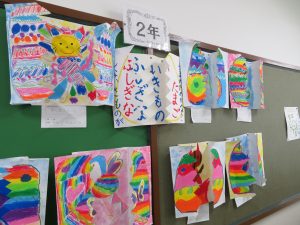 掲示板に「2年」と表示がされ画用紙にクレパスで綺麗に色塗りされたふしぎないきものの作品が8枚ほど掲示されている写真
