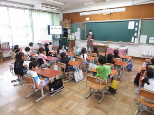 教室で子どもたちは自席についており、エプロンを付けた歯科衛生士さんが子どもたちの前に立って話をしている歯のみがき方教室の様子を後方より写した写真