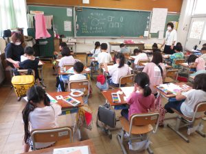 教室の自席に着いた子どもたちが、机の上にクレパスを置き画用紙を広げて、紫陽花の花を描いている様子を後方から写した写真