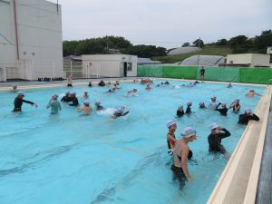 水の張ったプールの中で水泳帽をかぶり、水着を着た児童の皆さんが、泳いだり、友達と楽しそうに過ごしている様子を写した写真