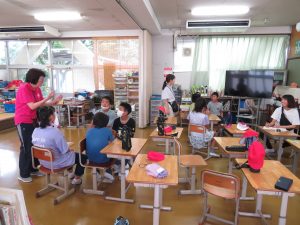 グループごとに分かれて座る生徒たちの横に先生が立ち、一緒に話し合いを行っている様子の写真