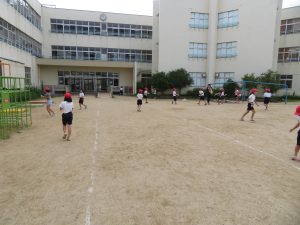 体操服を着た児童の皆さんがペットボトルを手に持ち、運動場を走り回っている水遊びの様子の写真