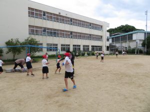 運動場で、先生に水をかけられ、逃げようとしている児童達が写っている水遊びの様子の写真