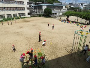 広々とした運動場で、ボール遊びをしている児童やジャングルジムなどの遊具で遊んでいる児童など、思い思いに運動場で遊んでいる児童が写っている様子の写真