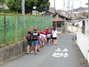 道路の左側をランドセルを背負った子どもたちが1列に並んで班下校をしている様子を後方より写した写真
