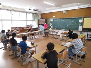 教室で机がロの字型に設置され、係の子ども達6名と先生方が席に着き、話し合いが行われている様子の写真