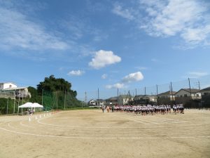 運動場の中央に児童の皆さんが整列して集まっている全体練習風景の様子の写真