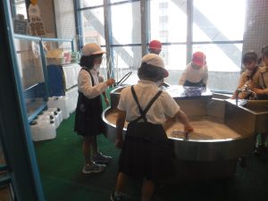仕切りのついた大きな容器の中に、手に持った輪っかの様な道具を容器に付けている子どもたちの写真
