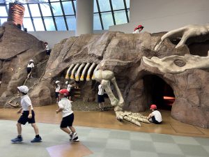 土に埋まった恐竜の骨を見立てて作られた遊具で、子どもたちが遊んでいる様子の写真