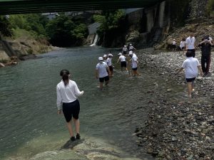 川に足をつけて遊んでいる子どもたちと、川岸に立っている先生たちの写真
