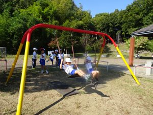 2人の児童が公園のブランコに座って、足を上に漕いで遊んでいる様子を写した写真