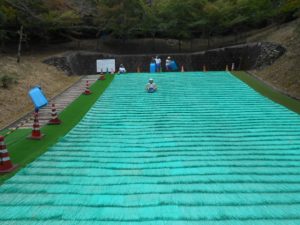 ちびっこゲレンデでそりに乗って芝滑りを楽しんでいる児童を写した写真