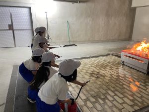 児童6人が消火器を使って、火災を想定した炎に向かって消火器のホースを向け、火を消そうとしている様子の写真