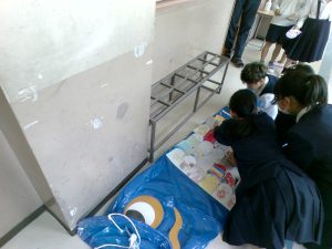 水色のビニール袋で製作した鯉のぼりのうろこ貼りを6年生が1年生に教えながら一緒に作業をしている様子を写した写真