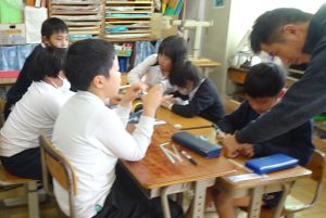 グループに分かれて座っている子どもたちが、一生懸命おもちゃ作りをしており、一人の男の子は男性に手伝ってもらいながら作業を進めている様子の写真