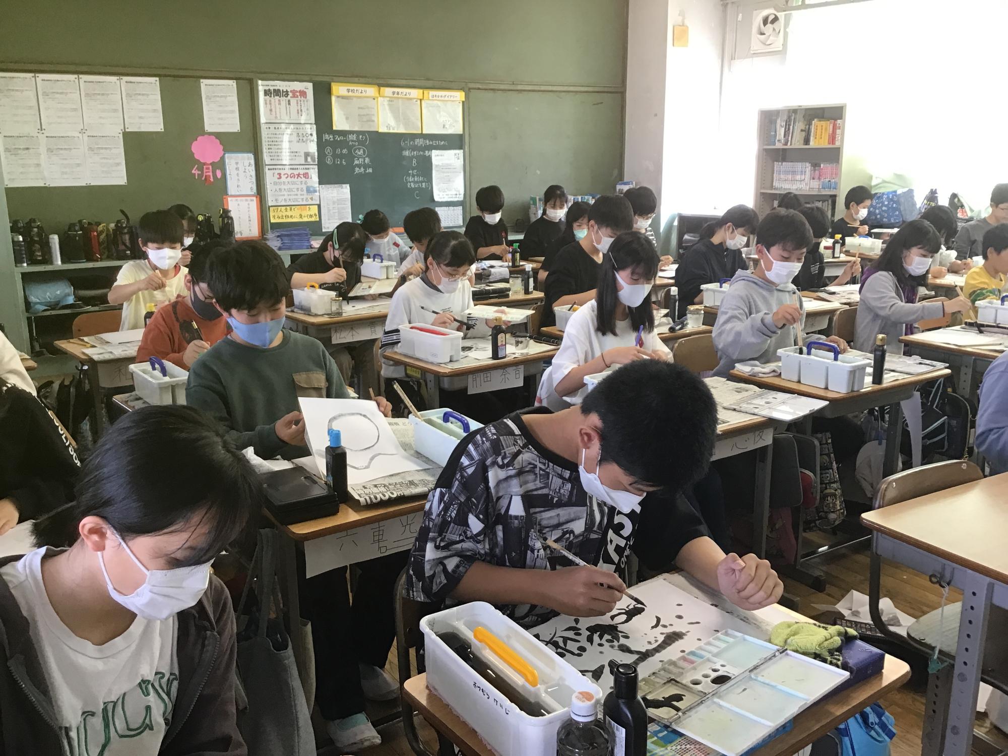 図工の授業で教室の自席に座っている児童たちが、真剣な表情で水墨画を行っている様子の写真