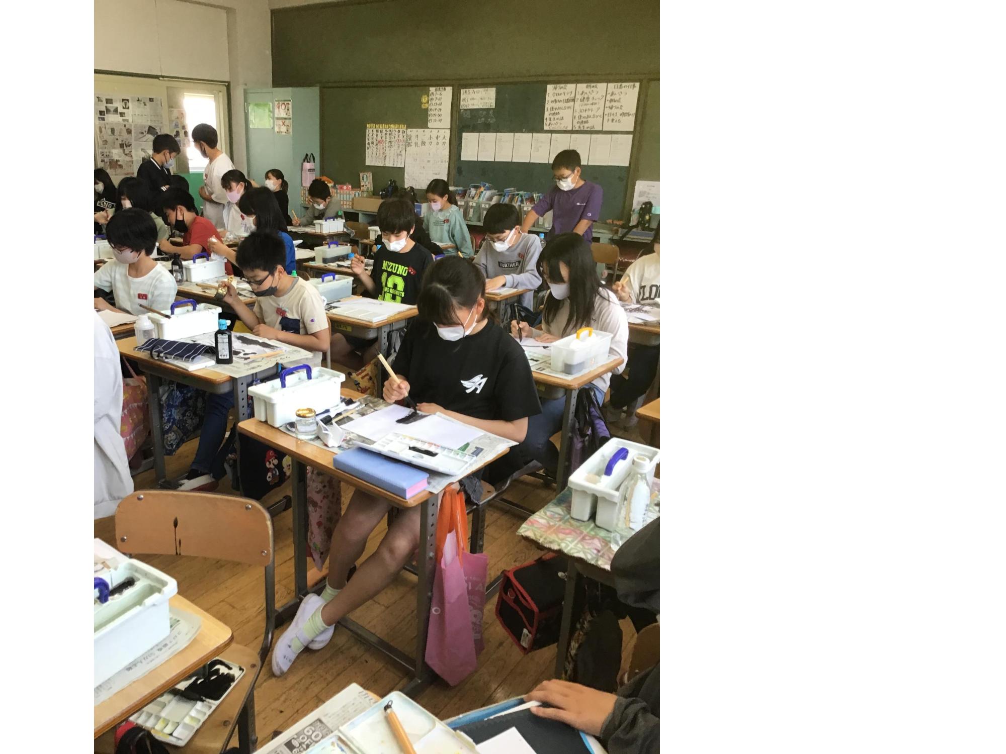 図工の授業中に教室で2名と1名の男子児童が席から立ち上がるなか、自席に座っている児童たちが真剣な表情で水墨画にチャレンジしている様子の写真