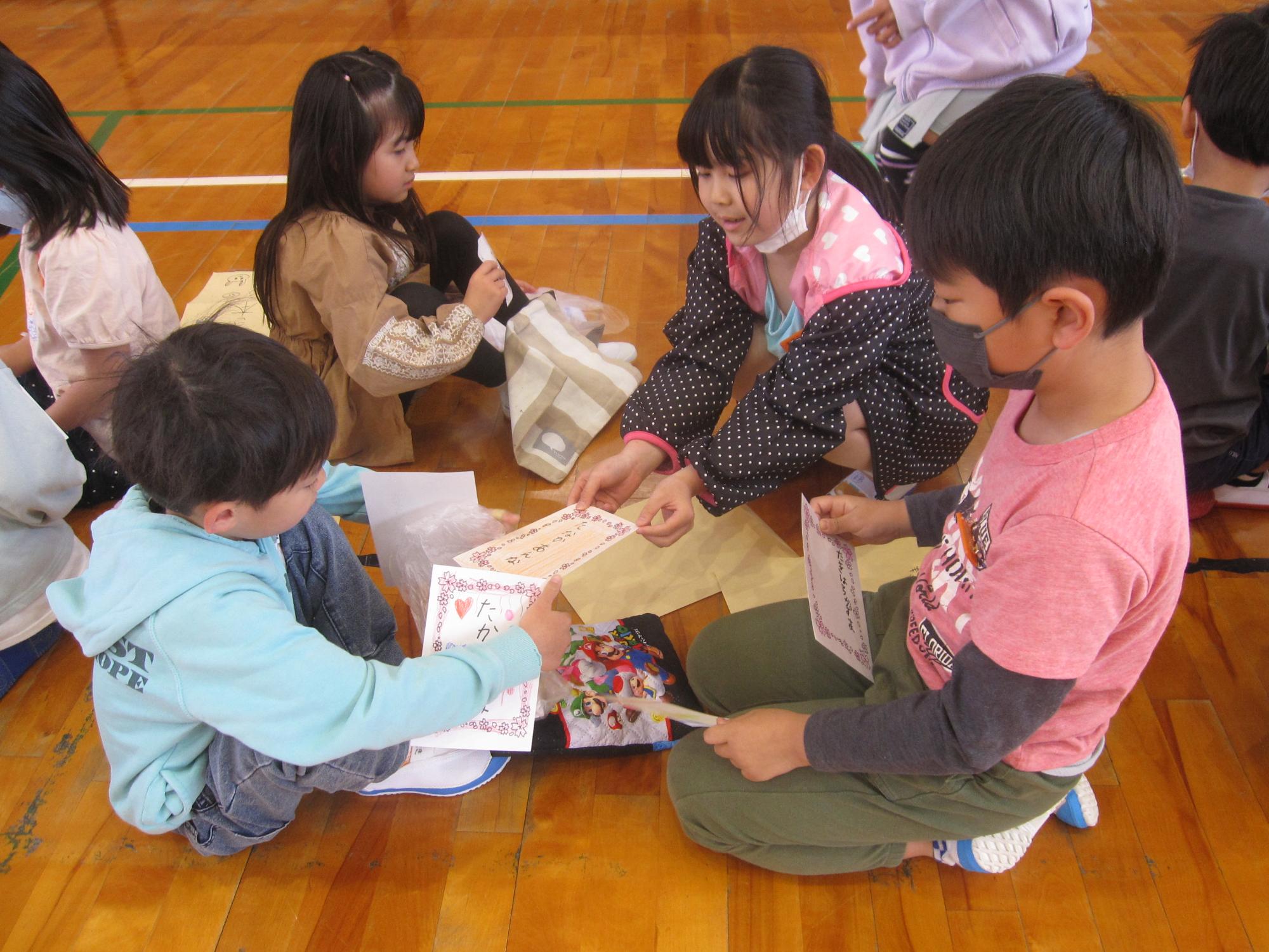 左側に座っている1年生の男子児童と女子児童の前に向かい合って座っている2年生の男子児童と女子児童が、名前が書かれたカードを交換しあっている初めましての会の様子の写真